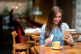 一个女人坐在餐厅的桌子上，手里拿着一张卡片和她的手机。