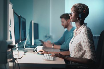 近距离侧视图的中期20金发黑人妇女做她的软件开发项目。她坐在台式电脑前，一边喝着咖啡，一边在电脑上工作。