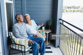 一对笑着的老夫妇坐在他们家的门廊上，俯瞰着水路