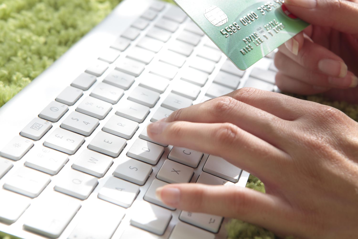 一个人一手在键盘上打字，一手拿着信用卡在网上购物