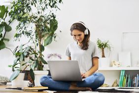 年轻女子坐在家里的地板上用笔记本电脑听音乐
