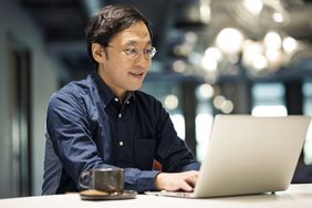 White man on computer with coffee mug on desk next to laptop