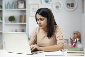 年轻女子在家庭办公室的笔记本电脑上打字
