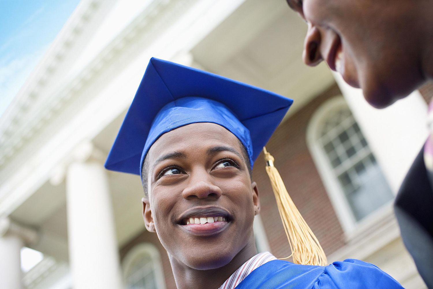 大学毕业生戴着蓝色的帽子，穿着蓝色的长袍，对着父母微笑