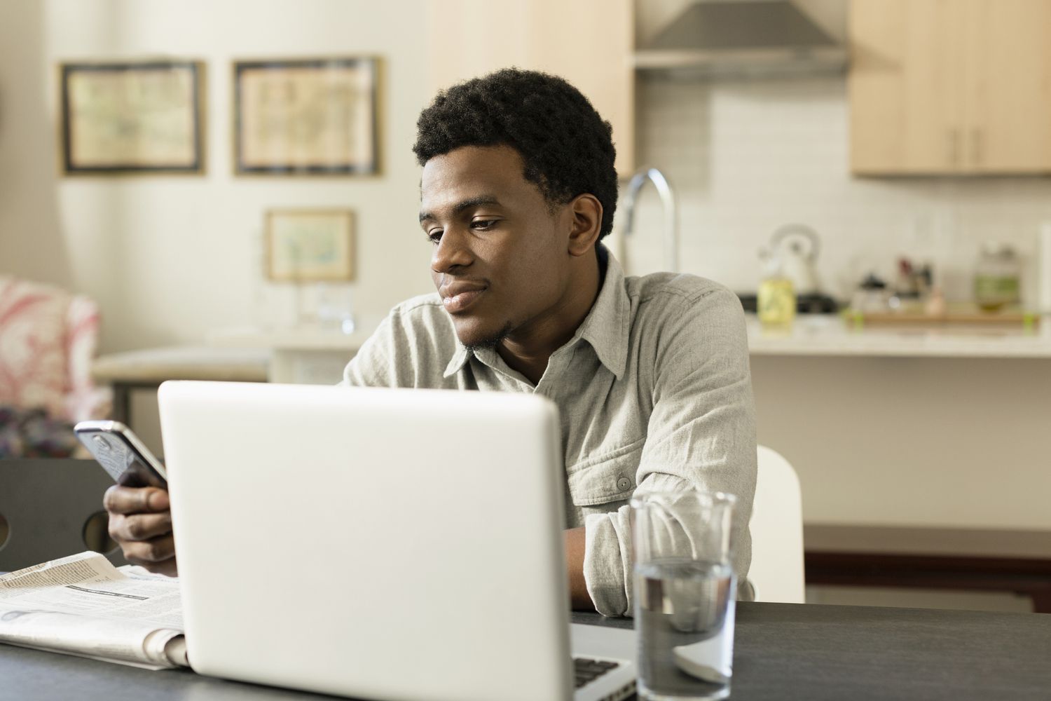 一名黑人男子在家里的笔记本电脑前用手机看新闻