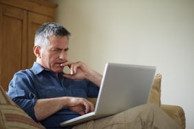 一个男人坐在沙发上疑惑的笔记本电脑放在他的大腿上。
