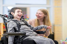 有特殊需要的小男孩坐在轮椅上和他的女看护人一起笑