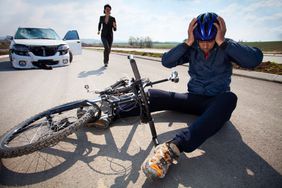 一名骑自行车的人被车撞后，戴着头盔坐在街上。汽车司机向他跑过来。