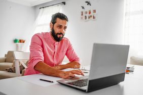 穿粉色衬衫的人在家里用笔记本电脑工作