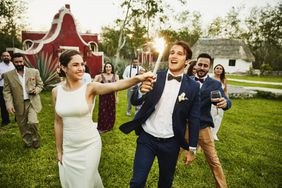 A bride and groom hold a sparkler while celebrating their wedding with guests.