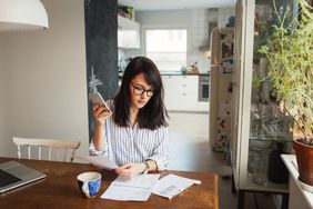 一个女人在家里的桌子上用电话、咖啡、文件来评估她的资产