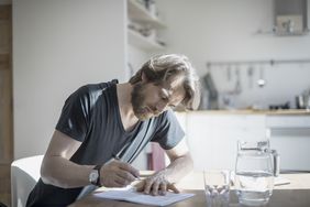 在一个干净明亮的厨房里，一个人坐在桌子旁填写表格。