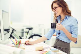 一个微笑的女人坐在白色的家庭办公桌前，手里拿着一杯咖啡