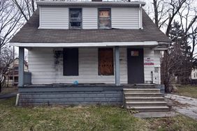 一个窗户被木板封住的破旧房子被当作银行拥有的REO财产出售。