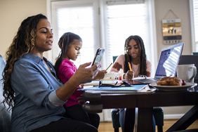 一位女士坐在电脑前，她的女儿们在桌旁做作业