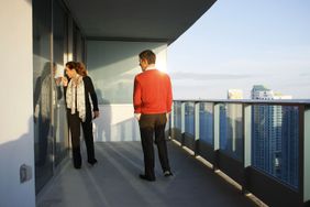 一对情侣站在高层阳台上，透过玻璃门往里看