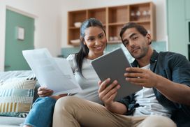 一对年轻夫妇在家里用平板电脑做文书工作的镜头＂width=