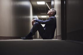 一名男子在收到被解雇的消息后，坐在走廊的地板上，一脸茫然
