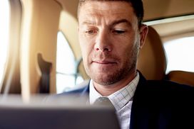 一位商人在开车时用平板电脑检查他的投资＂width=