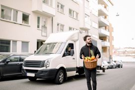 Young delivery driver carries wicker fruit basket in front of van