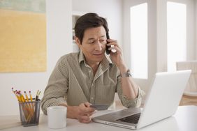 Man looking at laptop and reviewing his credit card information over the phone