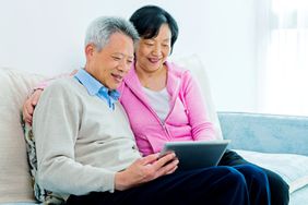 一对微笑的退休夫妇坐在沙发上，看着平板电脑
