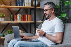 一个男人坐在沙发上，手里拿着咖啡杯，用笔记本电脑工作