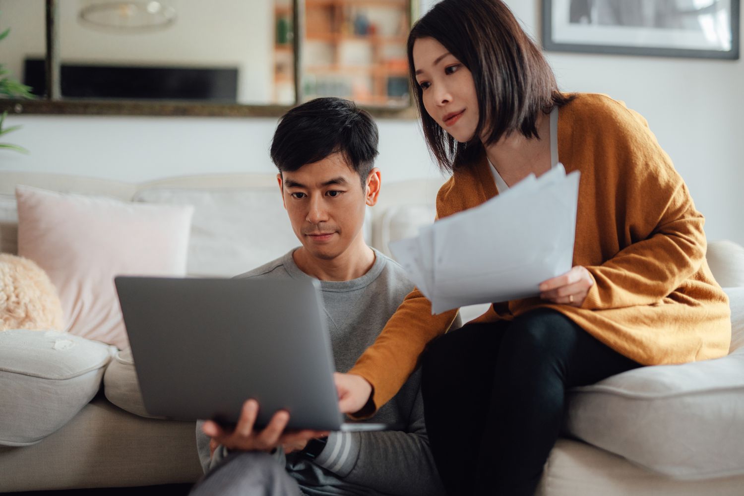 年轻的亚洲夫妇在沙发上用笔记本电脑讨论财务问题