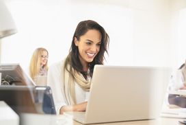 微笑的女人在办公室使用笔记本电脑”width=