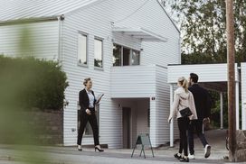 房地产经纪人在一栋新房子外和一对夫妇谈话”width=