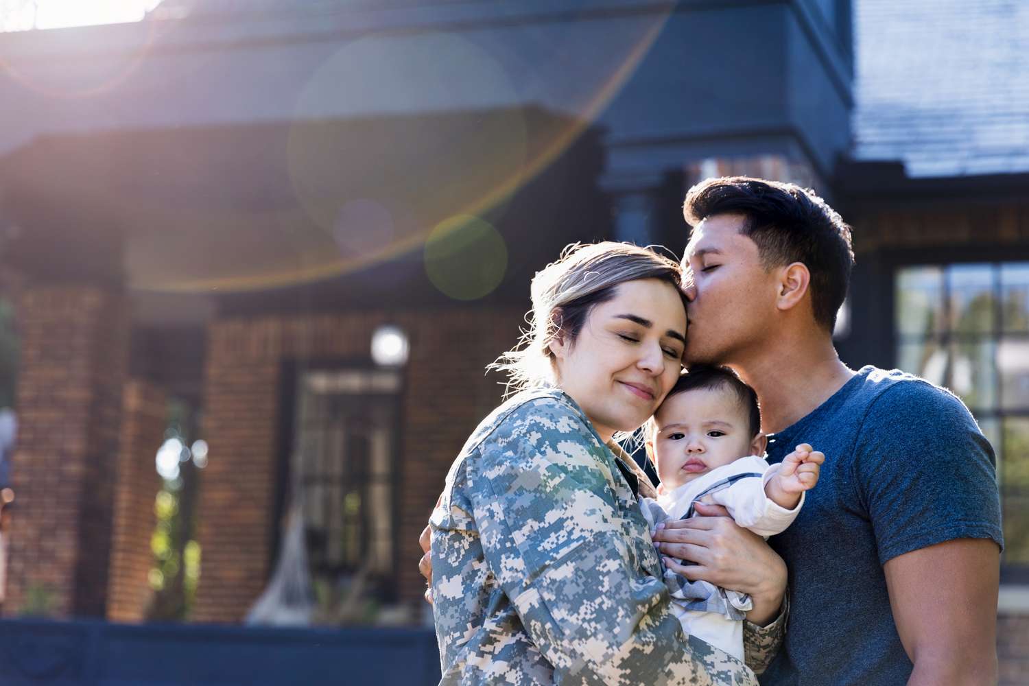 士兵抱着婴儿，丈夫亲吻她＂class=
