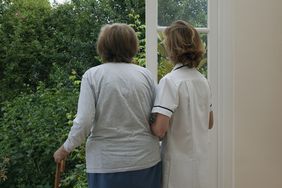 一位护士扶着一位站在敞开的门口的老妇人