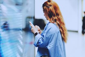 一名女子在地铁站的大触摸屏旁使用智能手机