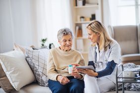 护理人员与一位老年妇女坐在床上讨论药物