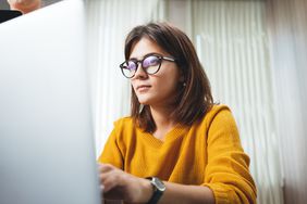 沉思的商业女人戴眼镜在办公室工作。年轻漂亮的女职工使用现代笔记本电脑
