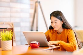 一个年轻的女人正在使用一台笔记本电脑在家舒舒服服地在客厅里。”width=