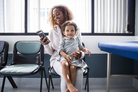 母亲蹒跚学步时使用智能手机在医生的办公室坐在大腿上”>
          </noscript>
         </div>
        </div>
       </div>
       <div class=