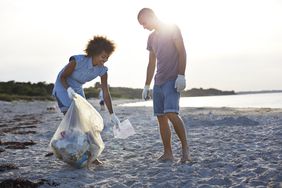 两个人站在海滩上捡垃圾，把它放进塑料袋