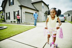 一个小女孩在一所房子前骑滑板车。