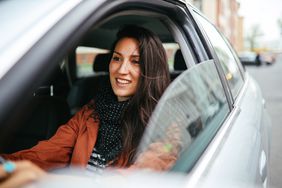 Smiling young woman drives a car with window down