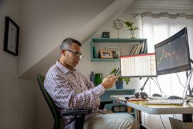 一名男子在家中办公室查看智能手机上的货币交易应用程序