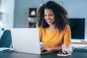 一位女士微笑着坐在打开的笔记本电脑前，双手放在键盘上。