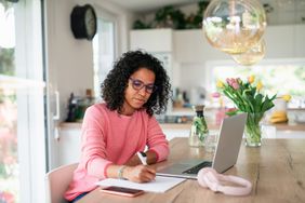戴眼镜的女人一边用笔记本电脑工作，一边在纸上写着什么＂>
          </noscript>
         </div>
        </div>
       </div>
       <div class=