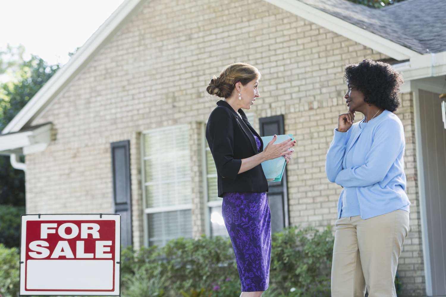 一个房地产经纪人站在一个挂着出售标志的房子前，和另一个女人交谈