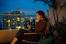 一名女子坐在阳台上的椅子上看她的智能手机