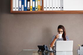 一个女人在办公室的笔记本电脑前喝咖啡
