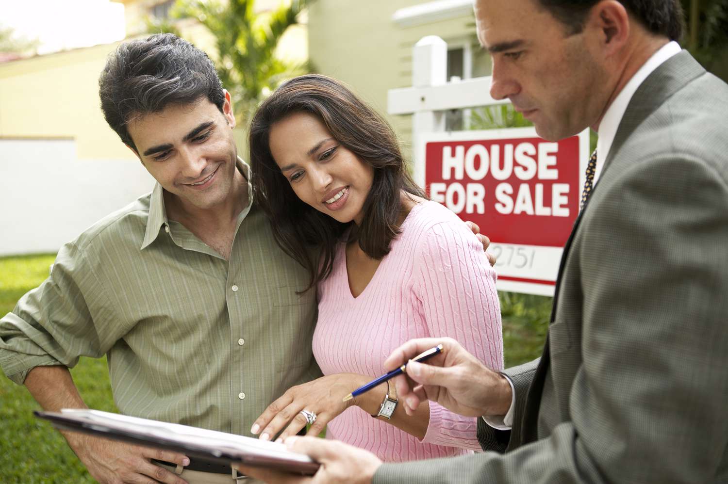 A couple talking to a real estate agent with paperwork outside a house for sale