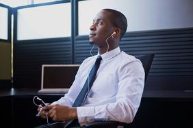 一个穿着正装衬衫打着领带的男人坐在办公室里，戴着耳机听电话
