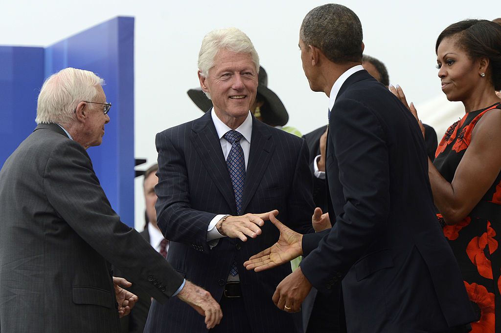 2013年8月28日，美国总统巴拉克·奥巴马(右二)与美国前总统比尔·克林顿(左二)握手，第一夫人米歇尔·奥巴马(右)和美国前总统吉米·卡特在华盛顿特区举行的“让自由之声响起”纪念活动中观看。