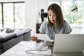 Asian woman going through bills at computer